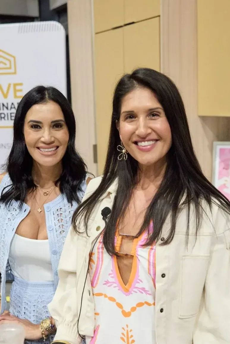 Two women smiling beside the Live Culinary Experience sign at a show kitchen stage
