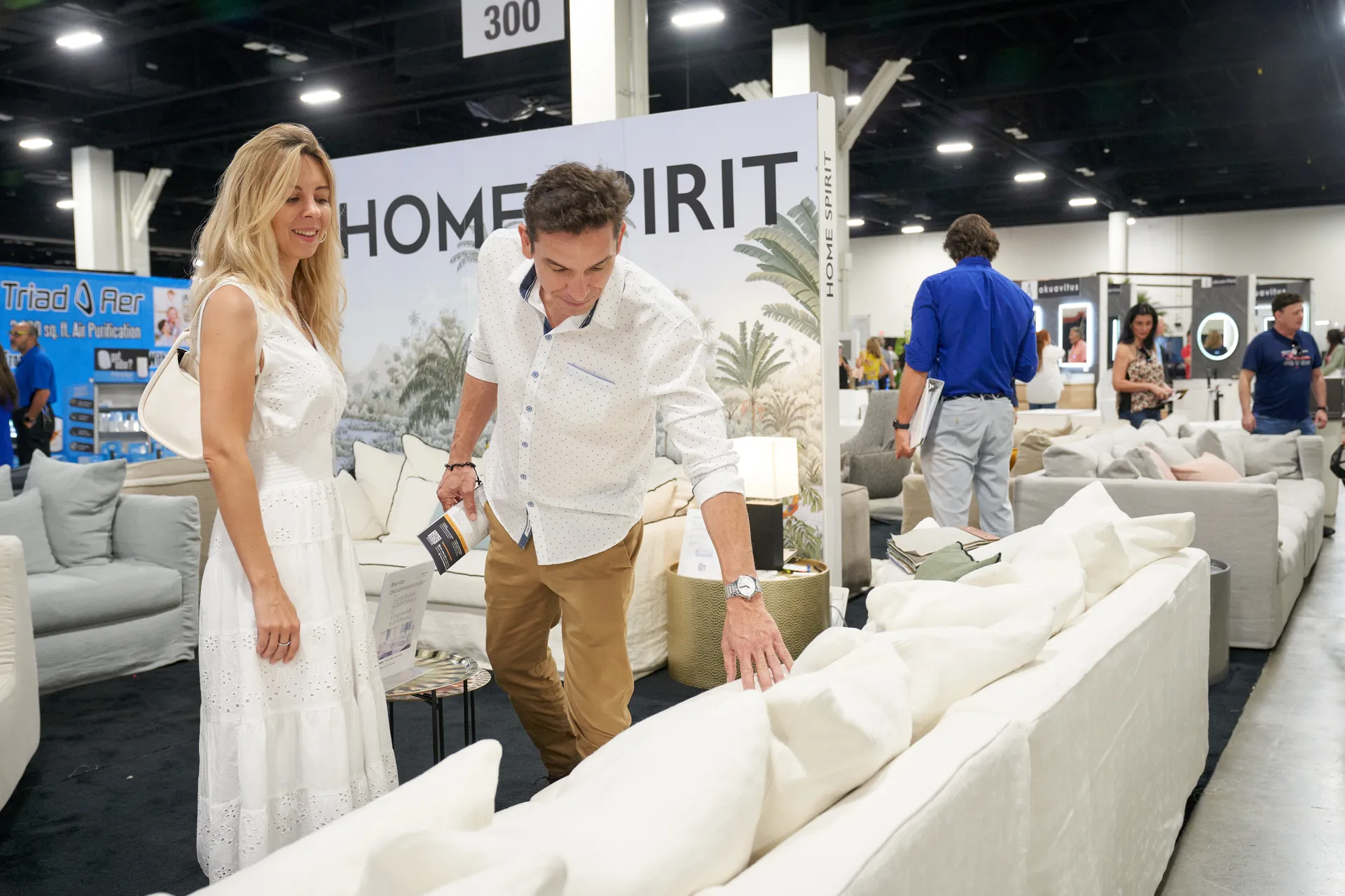 Attendee in a white cap chats with an exhibitor at a building materials booth with blue show bags