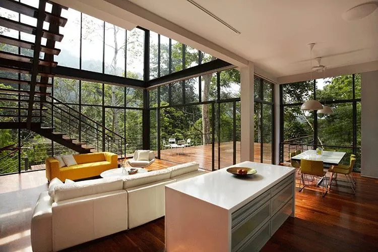 Contemporary open-plan interior with glass walls overlooking forested deck
